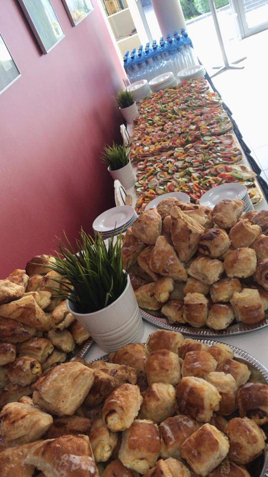 Stół z przekąskami: mini kanapki z warzywami i wędlinami, oraz tace z drobnymi wypiekami, udekorowany doniczkami z trawą.