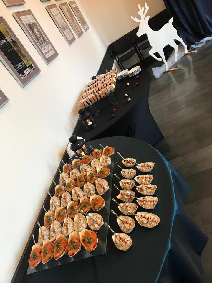 Elegancko przygotowany stół z przekąskami na przyjęciu: kanapeczki na szklanej tacy i sałatki w małych miseczkach z łyżeczkami, w tle dekoracja w postaci białego renifera.