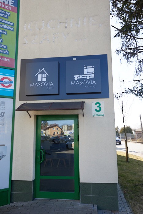 Wejście do biura firmy Masovia z szyldami oferującej usługi dla domu i transportu, widoczny numer budynku z adresem.