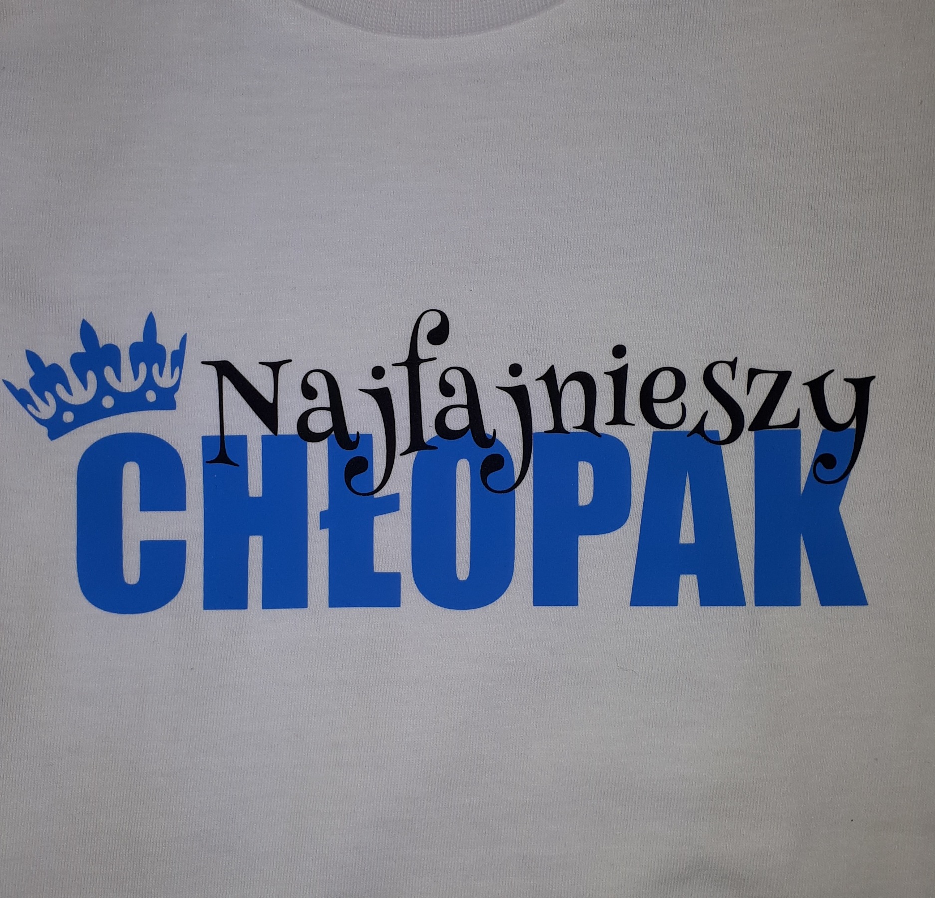 Biała koszulka z niebieskim nadrukiem korony i napisem 'Najfajniejszy CHŁOPAK' w dwóch różnych stylach czcionki.