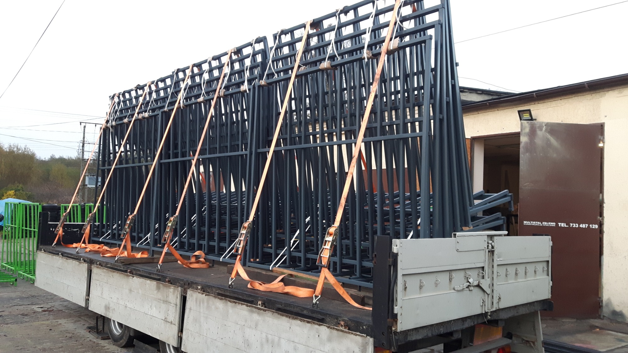 Stalowe konstrukcje szkieletowe zabezpieczone pomarańczowymi pasami transportowymi na platformie ciężarówki, gotowe do przewozu na plac budowy.