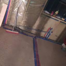 Wnętrze w trakcie instalacji wodno-kanalizacyjnej w surowym stanie, widoczne rury PEX w kolorach czerwonym i niebieskim prowadzone wzdłuż ścian i podłogi, zabezpieczone folią budowlaną, z widoczną...