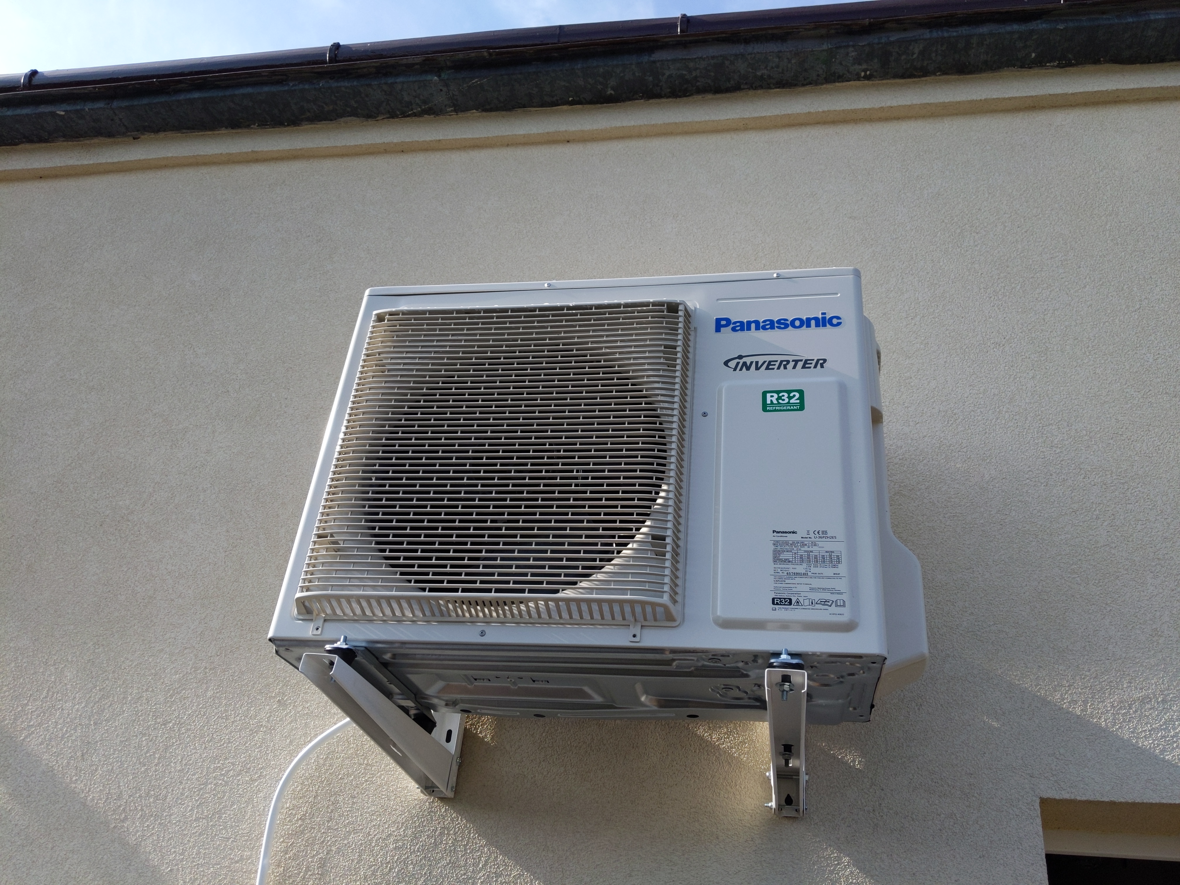 Zewnętrzna jednostka klimatyzacji Panasonic Inverter R32 zamontowana na elewacji budynku, widoczne metalowe wsporniki i przewody.