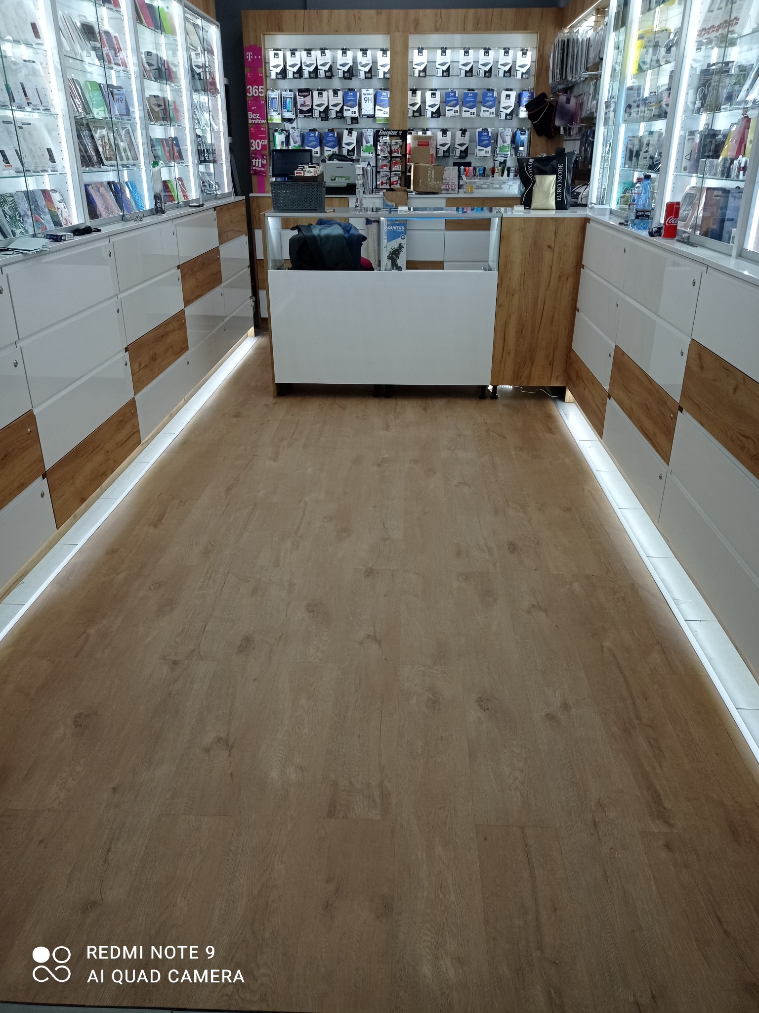 Jasna podłoga z paneli w sklepie z oświetleniem LED przy regałach. Widok na wnętrze sklepu z perspektywy podłogi. Ciepłe światło podkreśla strukturę drewna.