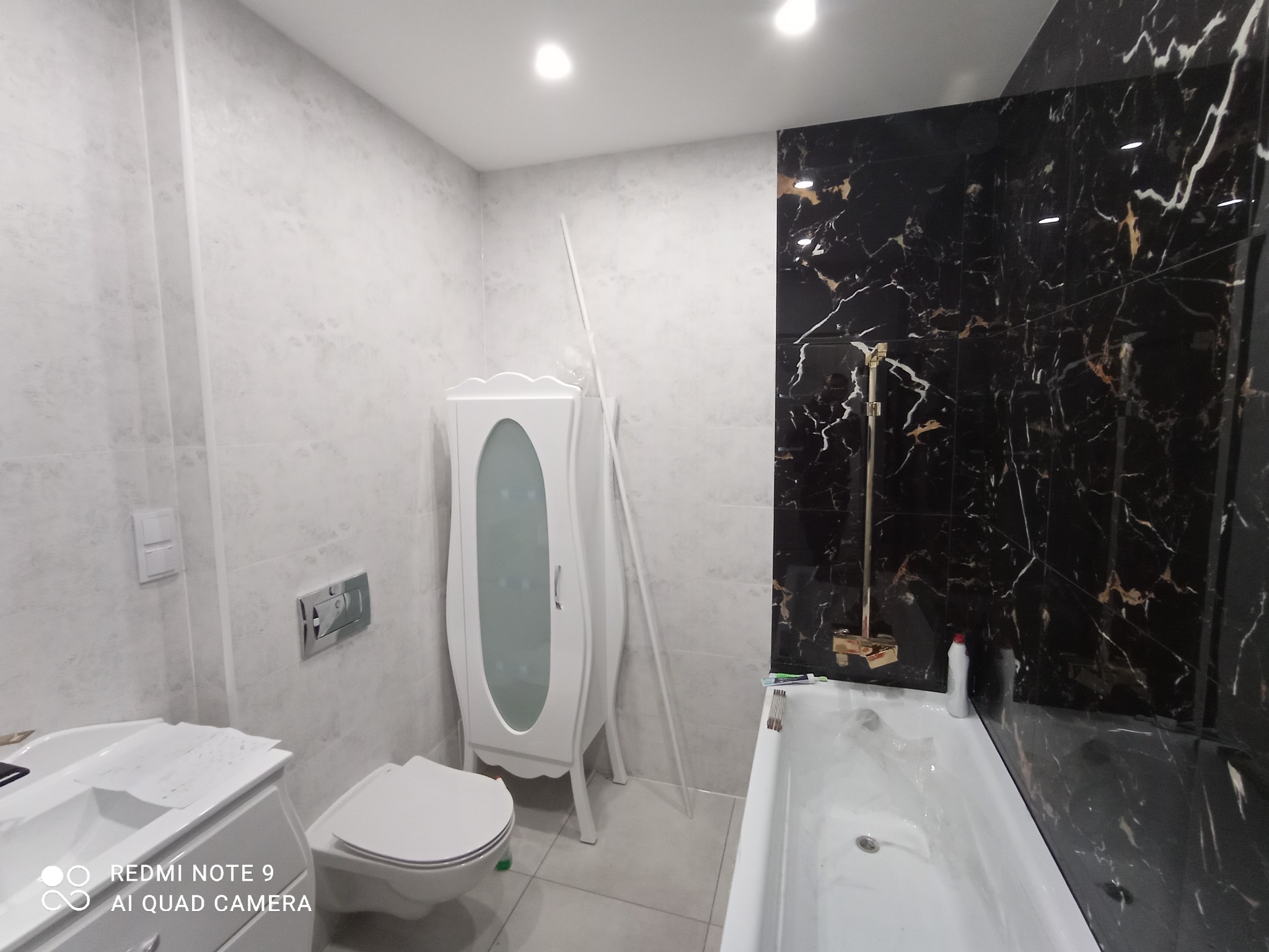 Wykończona łazienka z czarno-białymi płytkami, białą armaturą i szafką. Widoczne detale wykończeniowe i oświetlenie punktowe. Nowoczesny design.