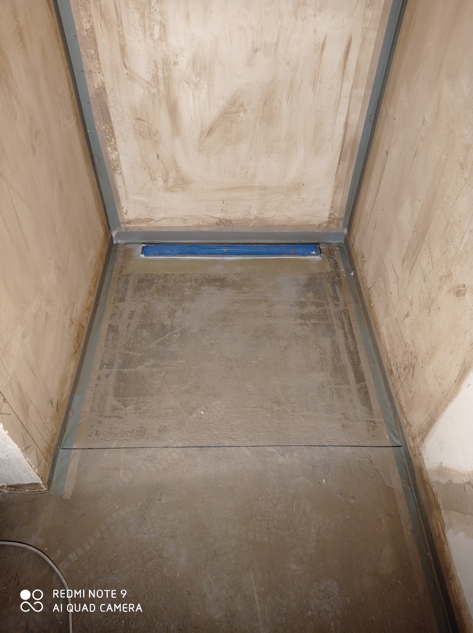 Przygotowane do dalszych prac wykończeniowych wnętrze kabiny prysznicowej z zamontowanym odpływem liniowym, widoczne ślady szpachlowania na ścianach i podłodze, zabezpieczone narożniki.