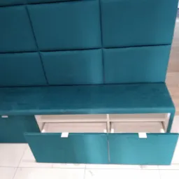 Turkusowa ławka tapicerowana z panelem ściennym i szufladami, otwarte dwie szuflady z białymi wnętrzami, biała podłoga z płytek.