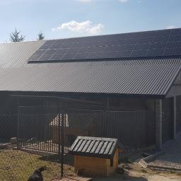 ARCHIGON Sp. z o.o. - Dom z ciemnym, metalowym dachem, na którym zamontowane są panele słoneczne. Widoczny również kojec dla psa i buda.