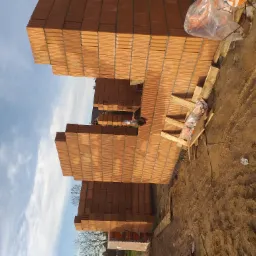 Wznoszone ściany fundamentowe z pustaków ceramicznych, widoczne zbrojenie i drewniane podpory, w tle błękitne niebo z chmurami.