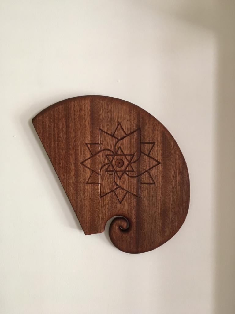 Dekoracyjny panel z ciemnego drewna z wygrawerowanym geometrycznym wzorem kwiatowym, przymocowany do białej ściany.
