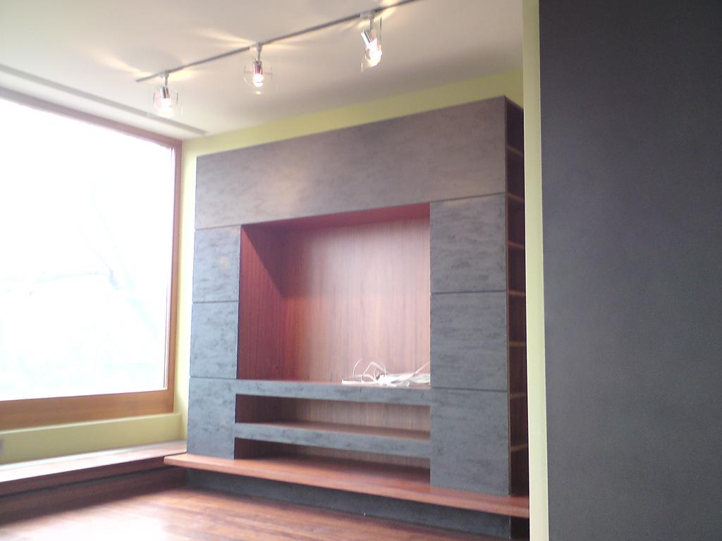 Wnęka telewizyjna z szarego kamienia z drewnianymi półkami, podświetlana reflektorami sufitowymi, widok z boku na parkiet i ścianę w kolorze grafitowym.