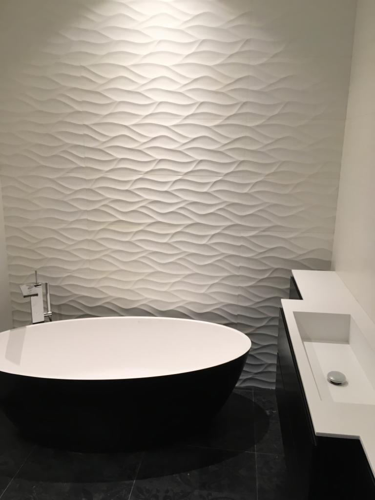 Nowoczesna łazienka z wolnostojącą wanną w kolorze czarnym, umywalką wpuszczoną w blat i ścianą z dekoracyjnych paneli 3D imitujących fale.