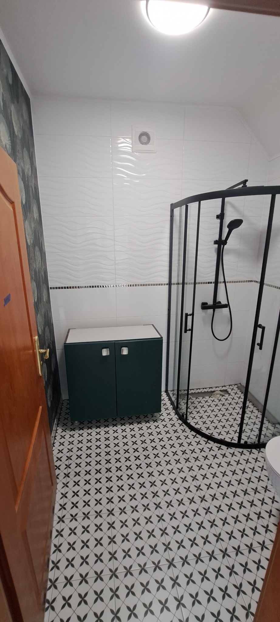 Wykończona łazienka z kabiną prysznicową z czarnymi ramami, szafką pod umywalkę w kolorze butelkowej zieleni i wzorzystymi płytkami podłogowymi w biało-czarne kwiaty.