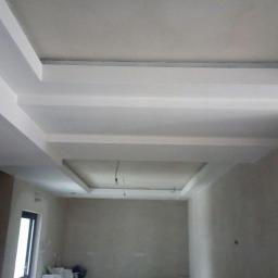 Kdkm - Wykończony sufit z dekoracyjnymi podwieszanymi elementami i oświetleniem w nowym wnętrzu, widoczne kable zwisające z jednego z podwieszeń.