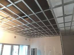 Metalowy stelaż sufitowy, widoczne płyty izolacyjne, przygotowanie do montażu okładziny, ściany w trakcie wykończenia.