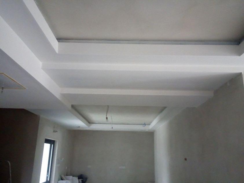 Wykończony sufit z dekoracyjnymi podwieszanymi elementami i oświetleniem w nowym wnętrzu, widoczne kable zwisające z jednego z podwieszeń.