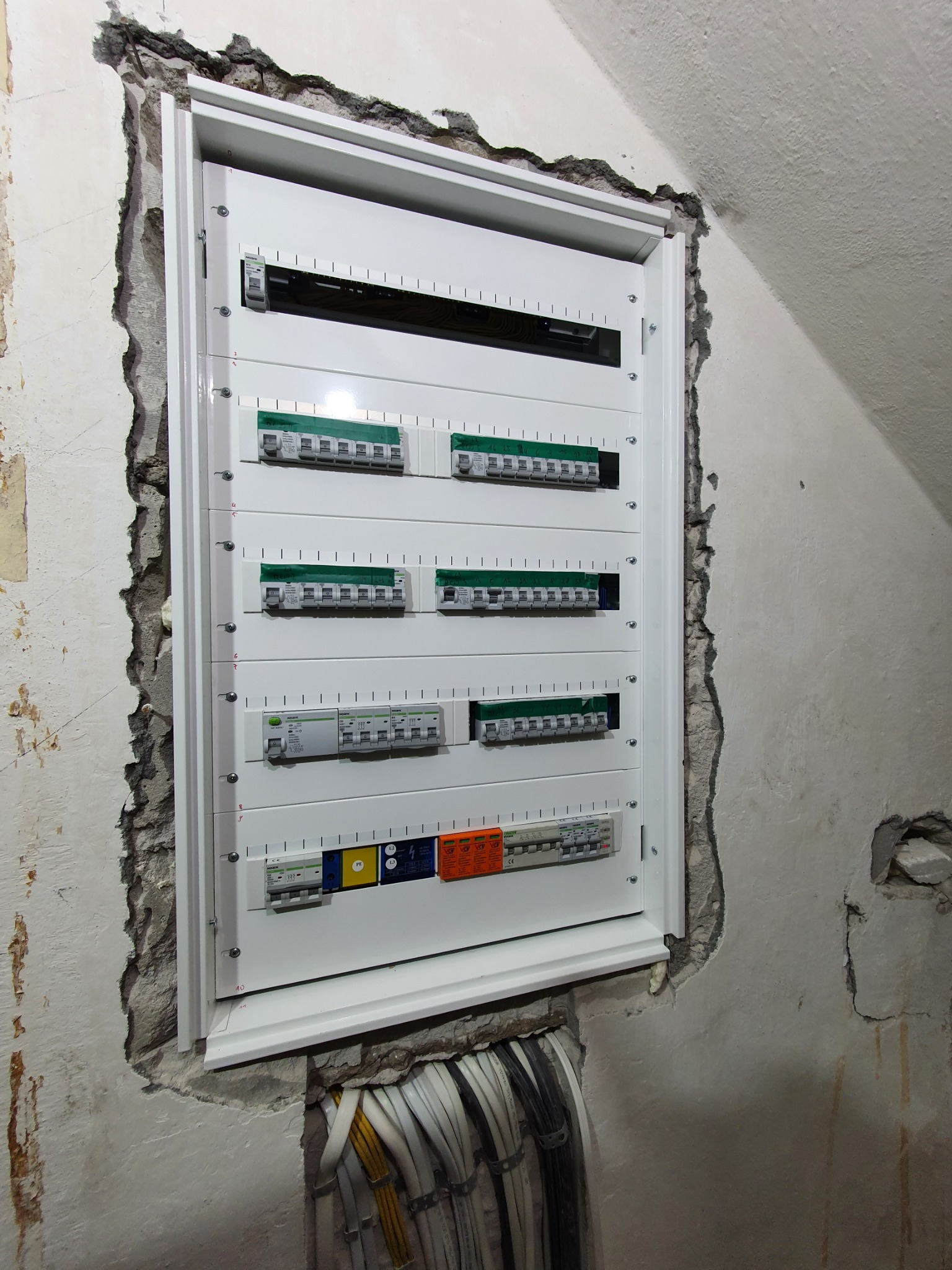 Nowa biała skrzynka z bezpiecznikami zamontowana w surowej ścianie z widocznymi przewodami elektrycznymi w peszlach.