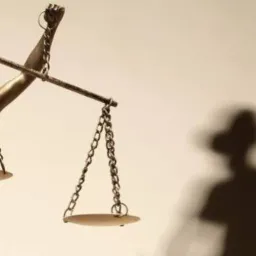 Statuetka Temidy z mieczem i wagą sprawiedliwości, rzucająca cień na ścianę.