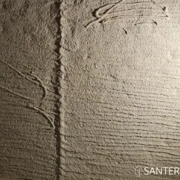 Surowa, szara ściana z wyraźną fakturą poziomych linii i nieregularnymi, wypukłymi wzorami. Pionowa szczelina dzieli powierzchnię, a w prawym dolnym rogu widoczne logo firmy Santerra.
