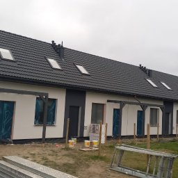 K . D INVEST Karol Damps Usługi ogólnobudowlane - Szeregowy budynek w trakcie wykończenia elewacji, okna zabezpieczone folią, widoczne puszki z farbą i rusztowanie.