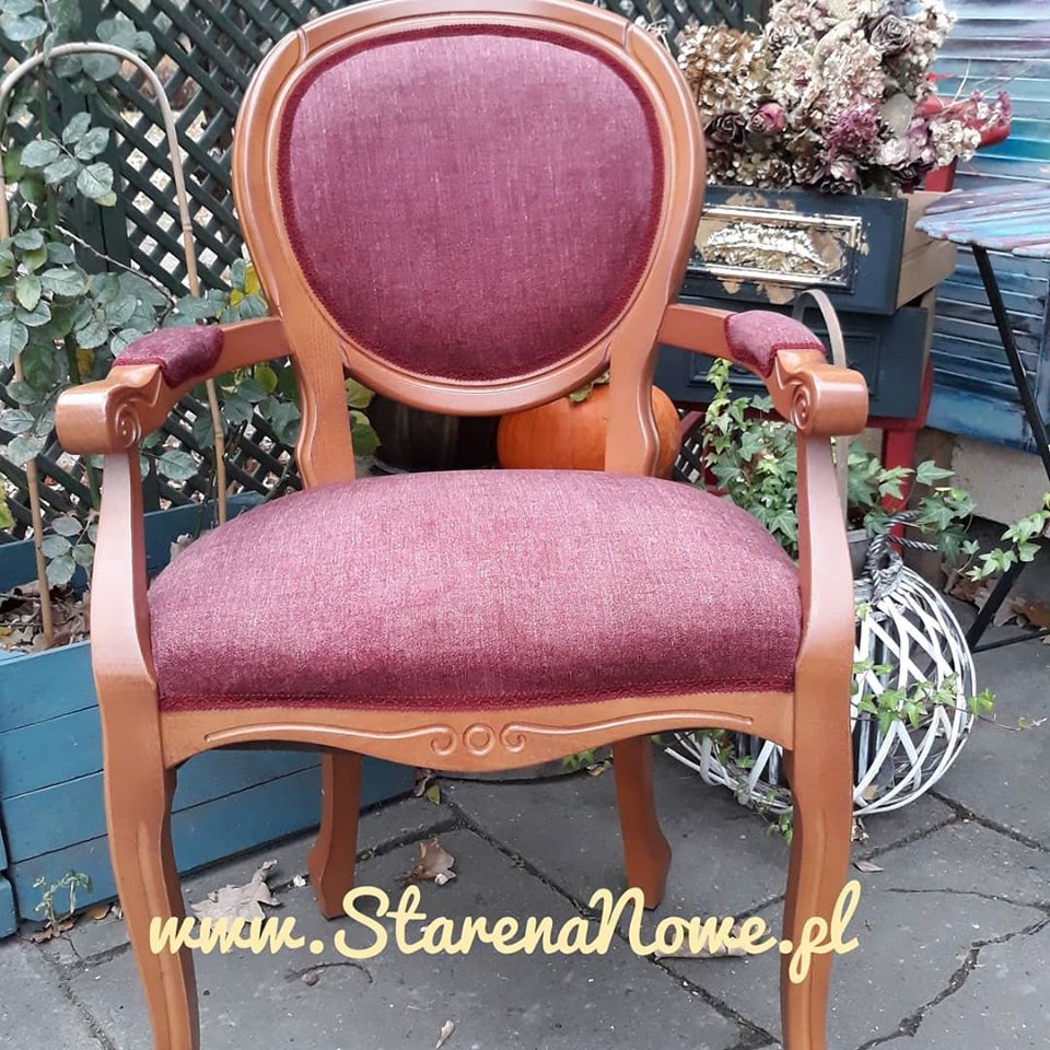 Odnowione krzesło w stylu retro z bordową tapicerką, ustawione na zewnątrz z dekoracjami jesiennymi w tle.