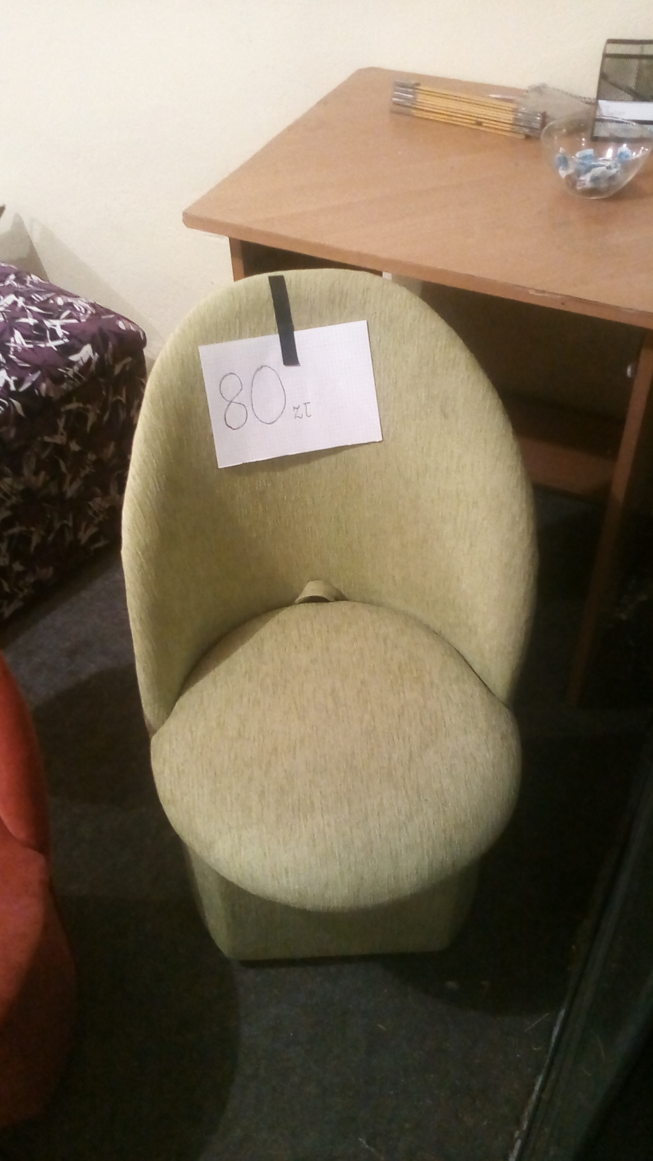 Używane krzesło tapicerowane w odcieniach zieleni z ceną 80 zł przypiętą kartką, widoczne obok inne meble.