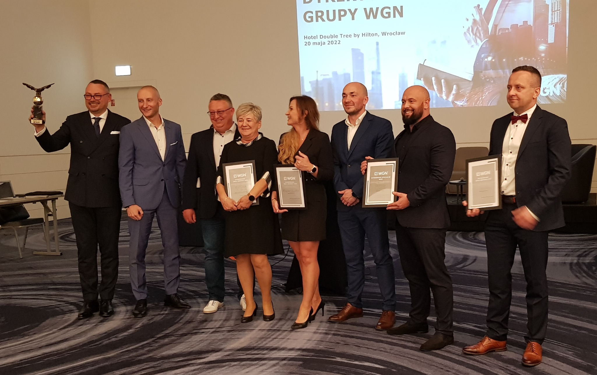 Grupa osób na scenie, trzymających certyfikaty WGN i statuetkę orła, podczas uroczystości w Hotelu Double Tree by Hilton we Wrocławiu, 20 maja 2022.