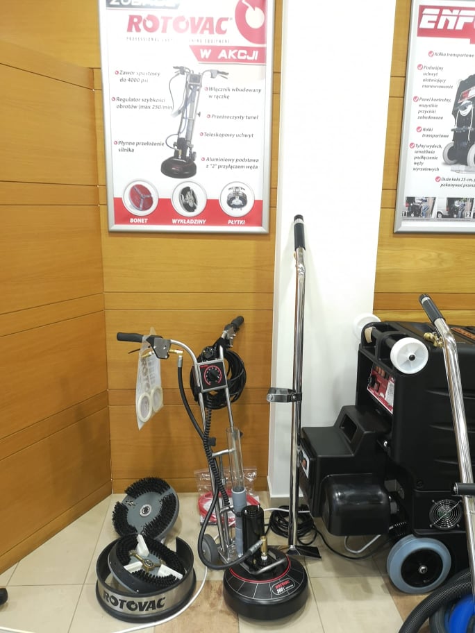Prezentacja profesjonalnych maszyn do czyszczenia podłóg Rotovac i Enforcer z akcesoriami, widoczne plakaty reklamowe z opisem funkcji.