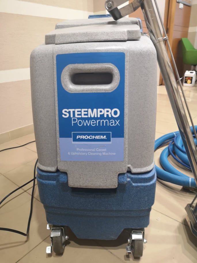 Profesjonalna maszyna do czyszczenia dywanów i tapicerki Steempro Powermax firmy Prochem z niebieskim wężem i metalową rączką, ustawiona na kafelkach.