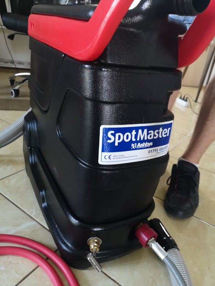 Profesjonalny, czarny odkurzacz piorący SpotMaster z czerwonymi elementami, widoczne węże i złączki, na podłodze z płytek.