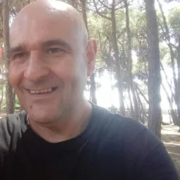 Portret uśmiechniętego mężczyzny na tle lasu sosnowego w słoneczny dzień.