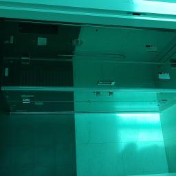 Arkadiusz Jurkowski - Szklana kabina prysznicowa z chromowanymi elementami, zamontowana w łazience z ciemnymi płytkami, oświetlona intensywnym, jednolitym światłem.