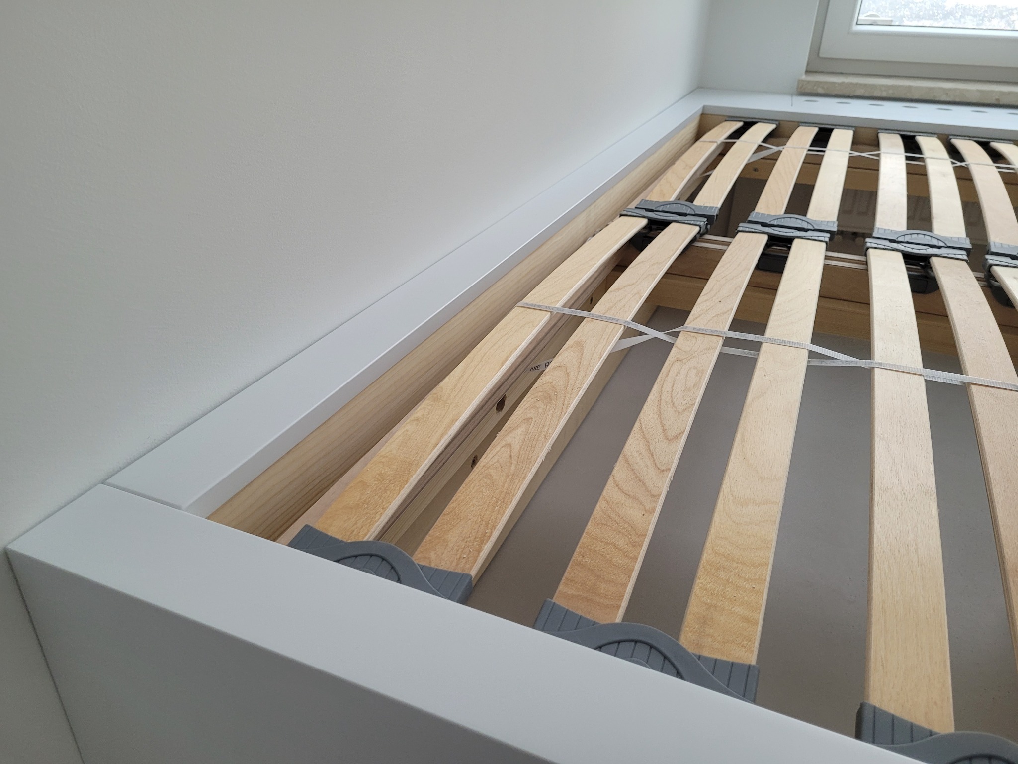 Stelaż łóżka z drewnianymi listwami, regulowane uchwyty, biała rama, widok od dołu, jasne światło.