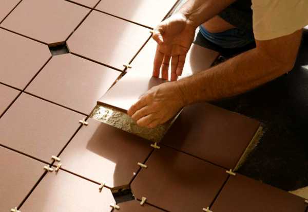 Układanie brązowych, heksagonalnych płytek podłogowych z użyciem krzyżyków dystansowych i widoczną warstwą kleju.