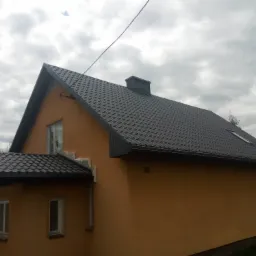 Dom jednorodzinny z nowym, ciemnoszarym dachem z blachodachówki, widoczne obróbki blacharskie, komin i numer domu '28'.