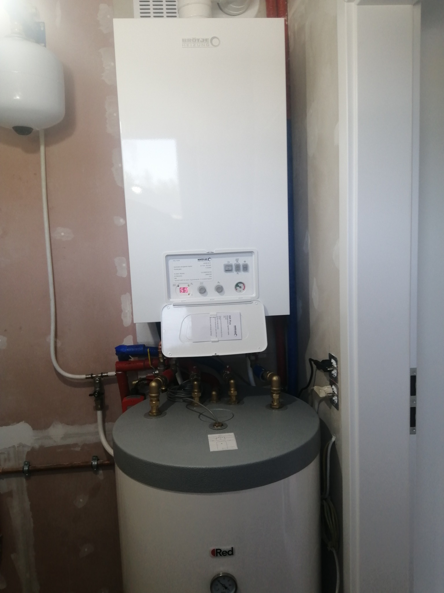 Biały piec grzewczy Brötje z podgrzewaczem wody Red, zamontowany na ścianie z widocznymi śladami szpachlowania, obok biała szafa.