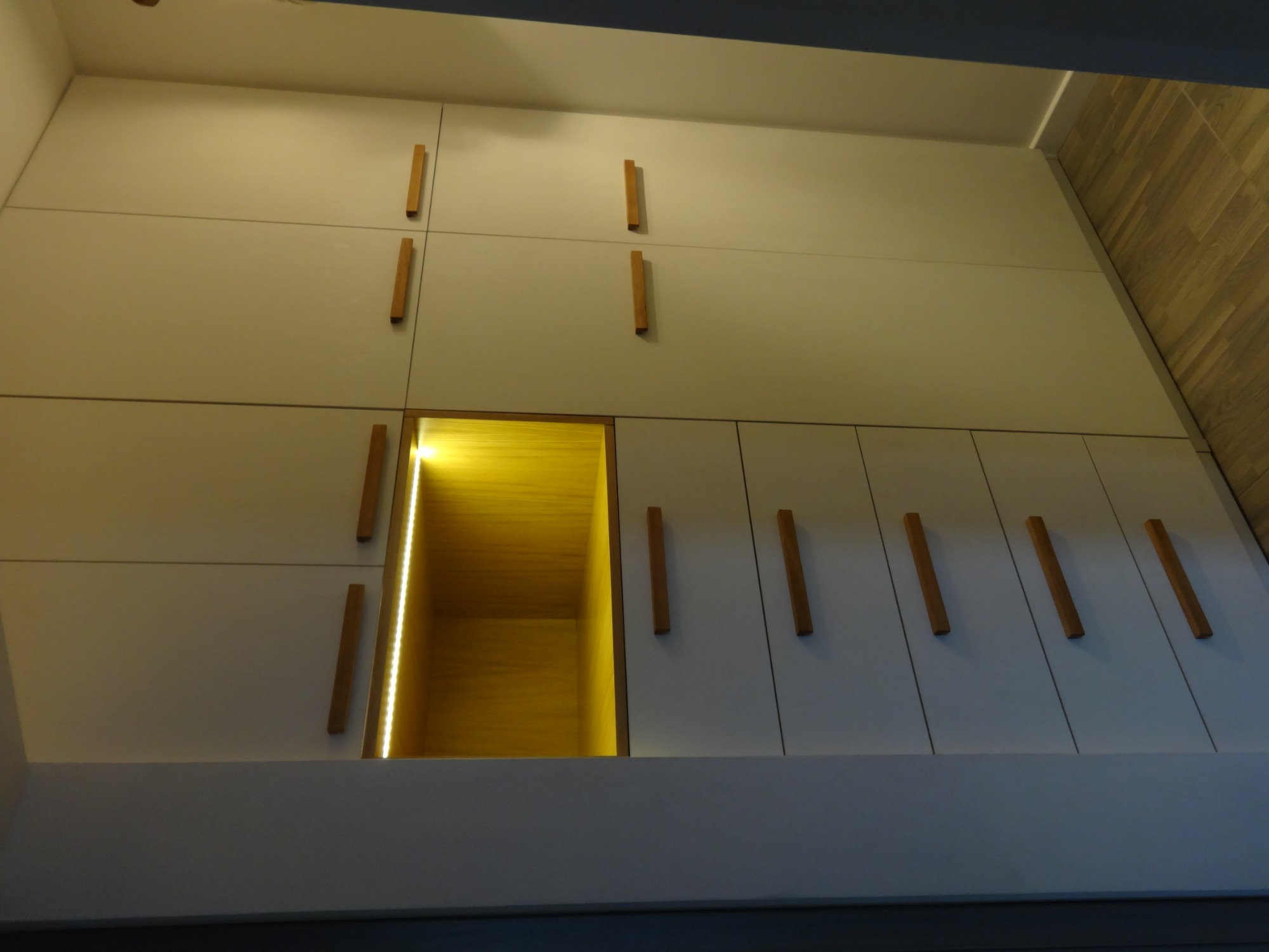 Biała szafa wnękowa z drewnianymi uchwytami i podświetlaną wnęką, widok od dołu.