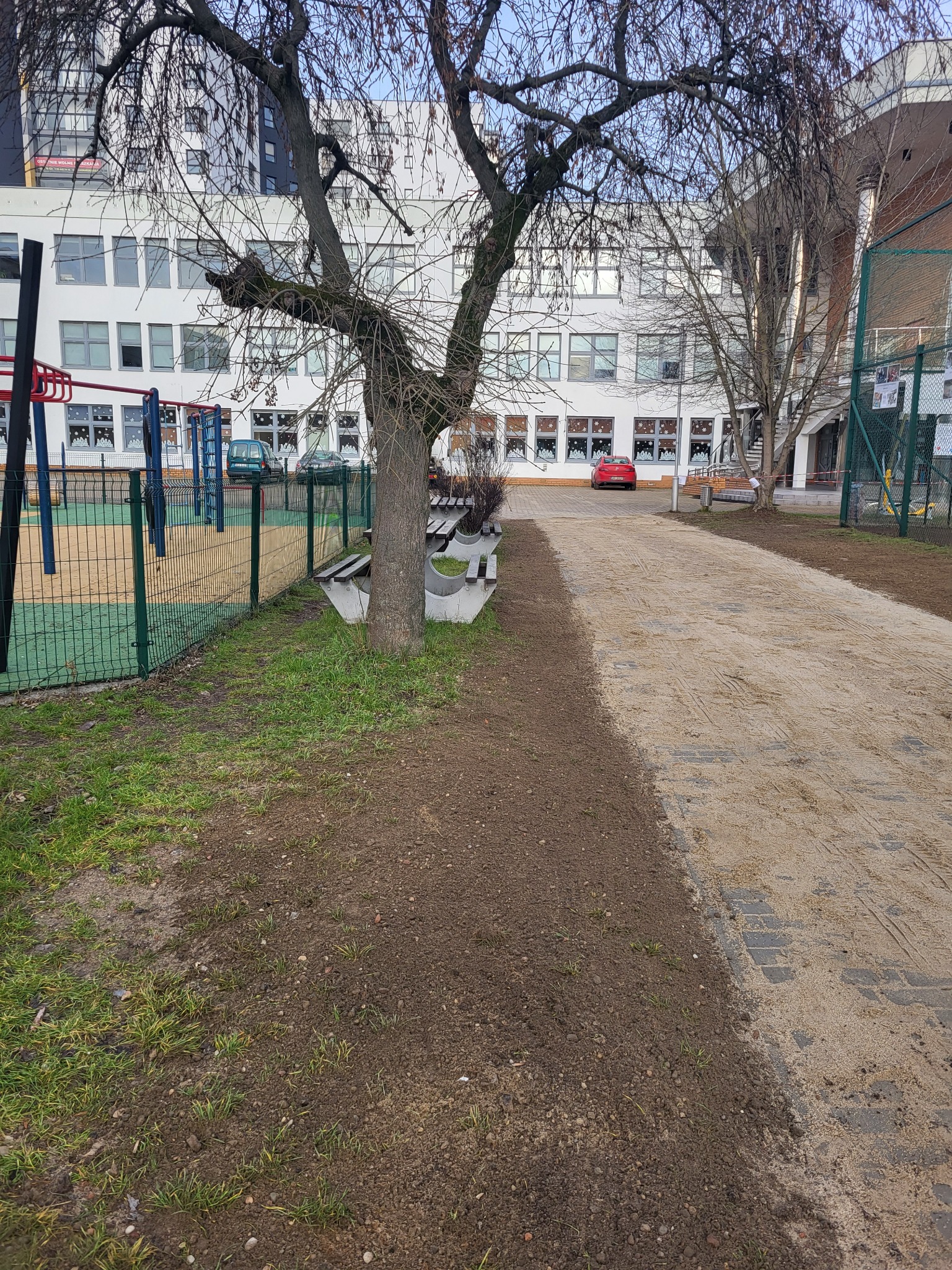 Przygotowany teren pod budowę z widocznym wyrównanym podłożem, częściowo utwardzoną drogą i placem zabaw w tle.