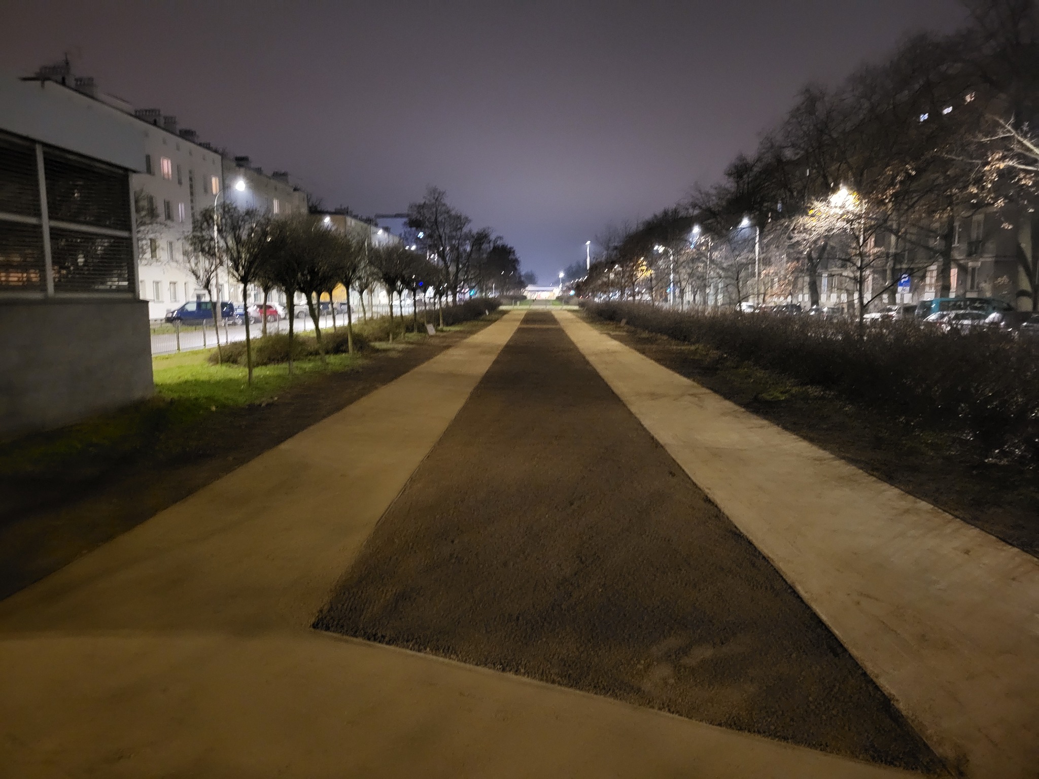 Nowa ścieżka z utwardzoną nawierzchnią wzdłuż ulicy, widok nocą z perspektywy pieszego, oświetlona latarniami ulicznymi.