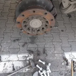 Demontaż koła ciężarówki z widoczną tarczą hamulcową, śrubami i narzędziami na brukowanej powierzchni.