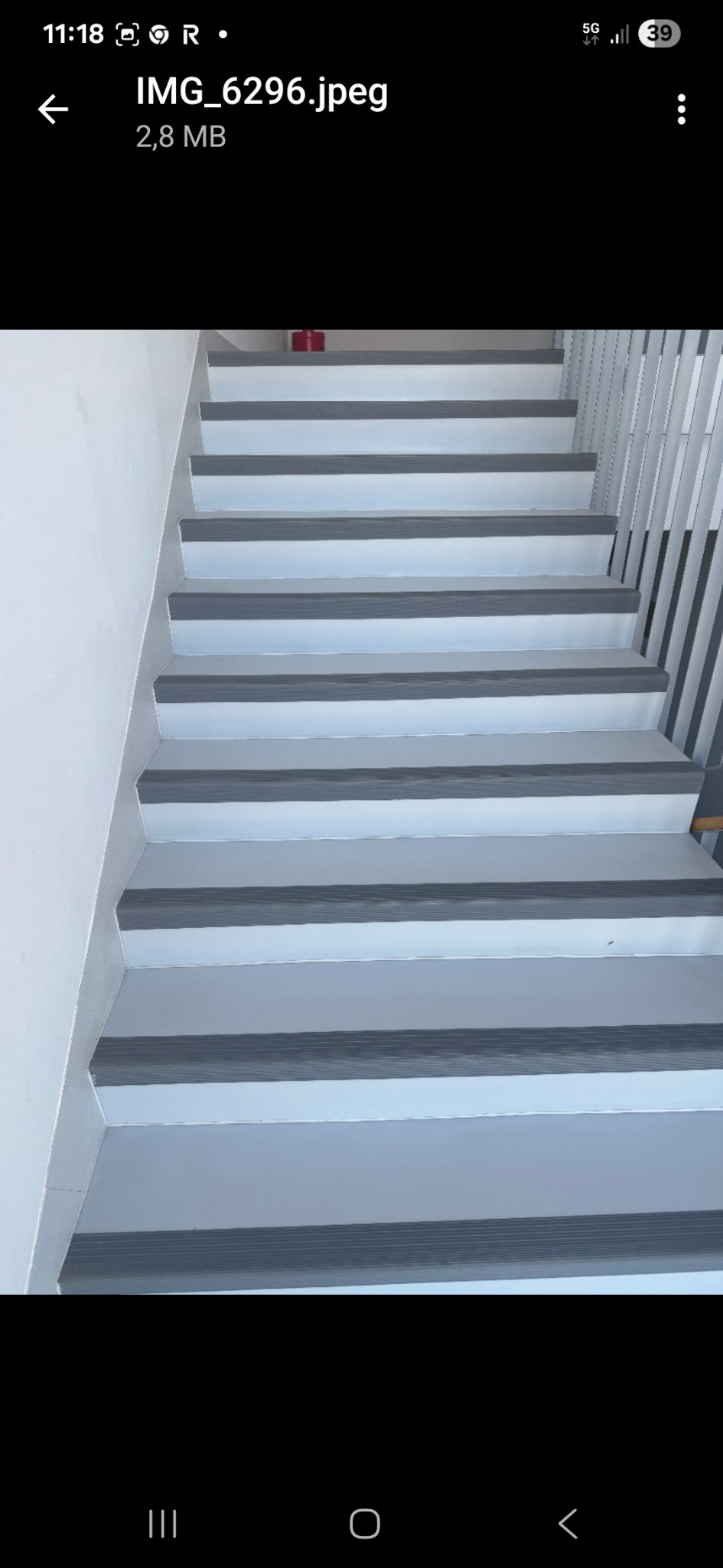 Schody po remoncie z szarymi nakładkami antypoślizgowymi na stopniach i białą farbą na ścianach, widok z dołu.