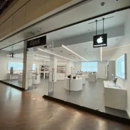 Eleganckie wnętrze salonu iSpot z jasnymi ścianami, minimalistycznymi białymi meblami ekspozycyjnymi i szklaną fasadą, widoczne logo Apple Premium Reseller.