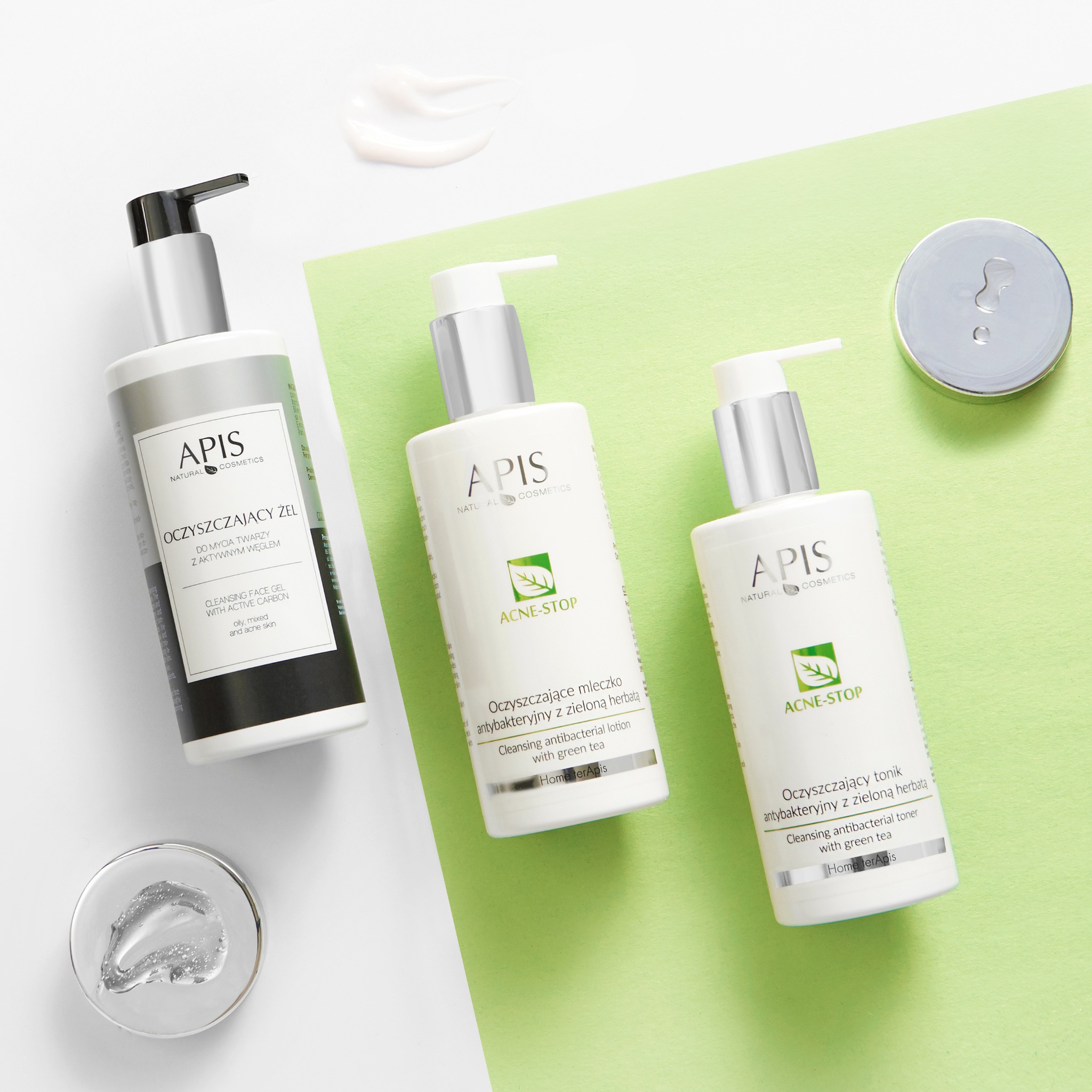Zestaw kosmetyków Apis Acne-Stop na zielono-białym tle: żel do mycia twarzy z węglem aktywnym, mleczko oczyszczające i tonik antybakteryjny z zieloną herbatą, oraz próbka kremu i żelu.