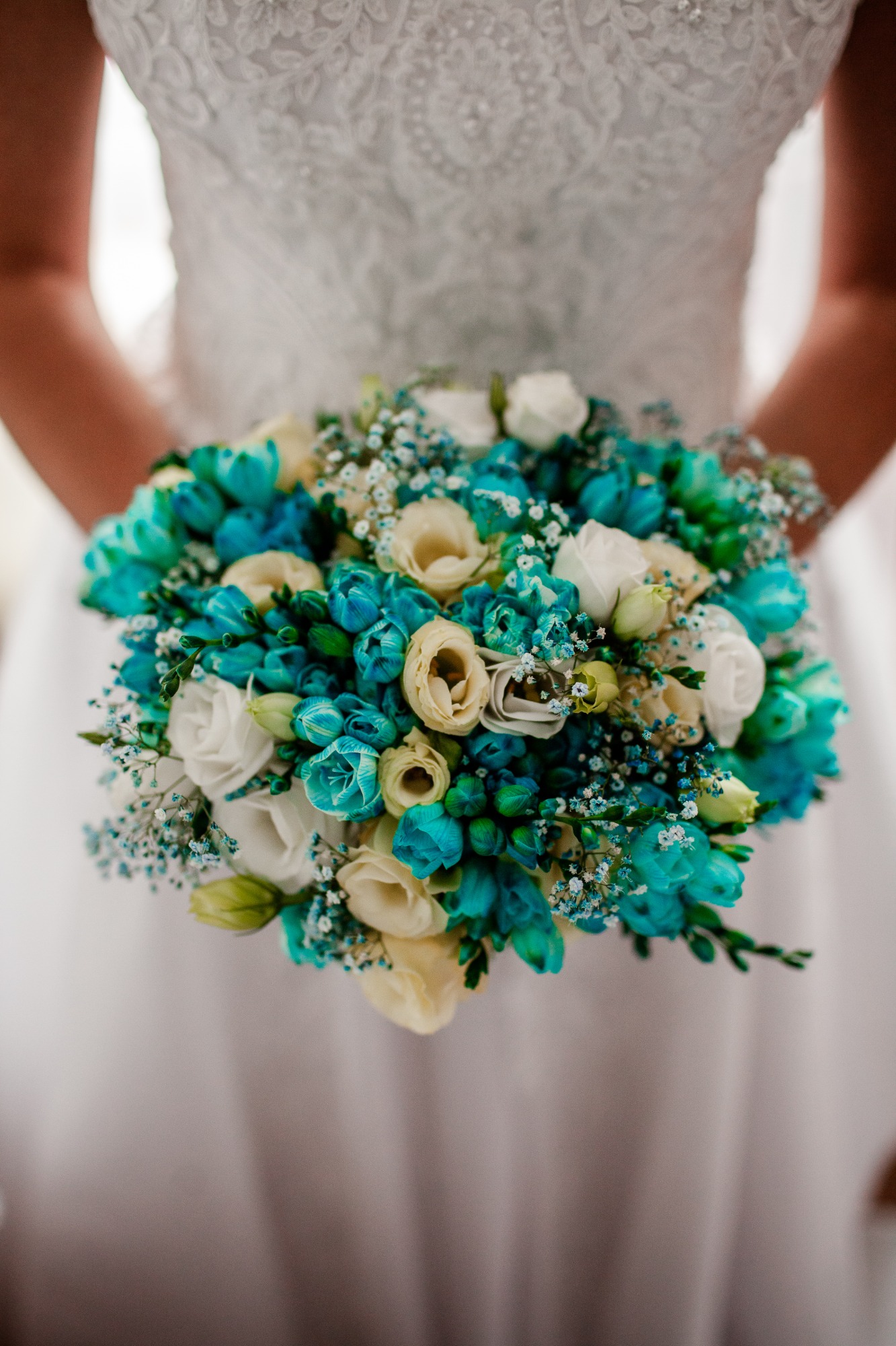 Panna młoda trzymająca bukiet ślubny z białych róż i turkusowych tulipanów, uzupełniony drobnymi białymi kwiatami gipsówki.