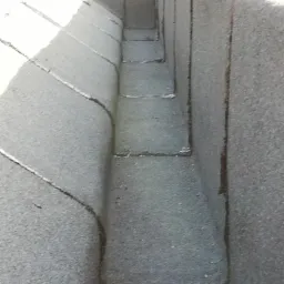 Szczegółowe ujęcie uszczelnienia połączenia dachu z attyką, widoczne warstwy papy bitumicznej z wyraźnymi liniami łączeń i miejscami zalania masą bitumiczną.