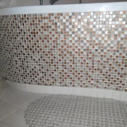 Mozaika z beżowo-brązowych płytek zdobi obudowę wanny, na podłodze antypoślizgowa mata z przyssawkami.