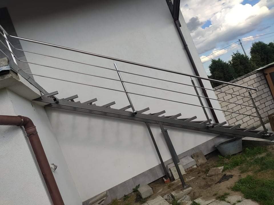 Zewnętrzna konstrukcja schodów z metalu z nierdzewną balustradą, widok z boku, niedokończone otoczenie.