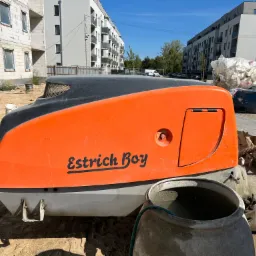 Pompa do jastrychu 'Estrich Boy' na placu budowy z widokiem na nowe budynki mieszkalne i kontener na śmieci.