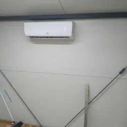 Biały klimatyzator marki CH zamontowany na ścianie z paneli w pomieszczeniu przemysłowym, widoczne stalowe elementy konstrukcyjne i poziomica oparta o ścianę, podłoga częściowo przykryta folią.