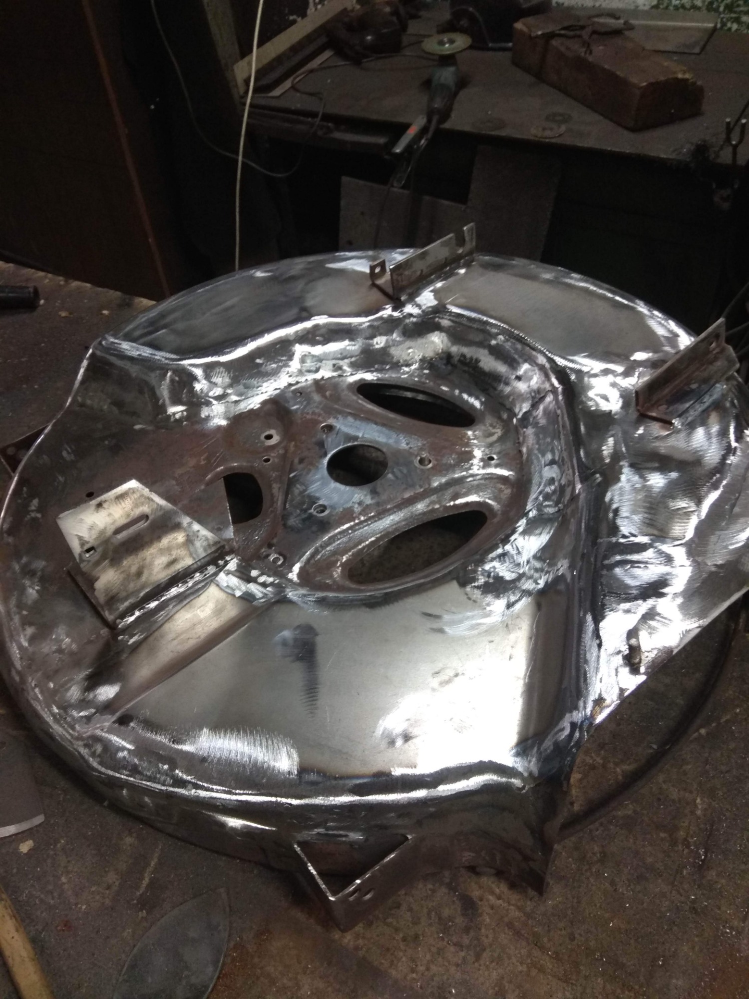 Metalowa konstrukcja z otworami i przyspawanymi elementami, prawdopodobnie w trakcie obróbki lub budowy, widoczne ślady spawania i obróbki mechanicznej, na warsztatowym stole.